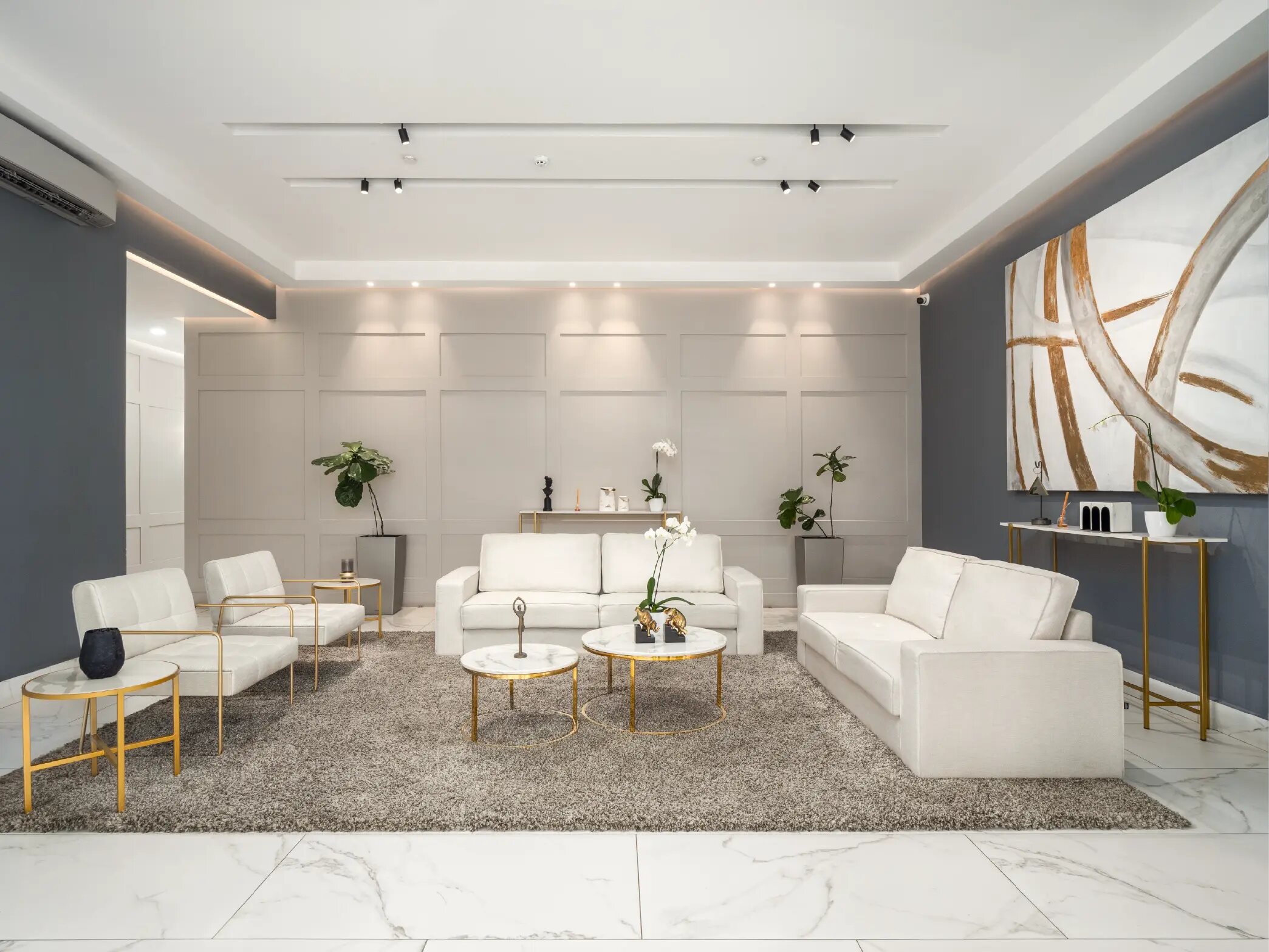 Lobby moderno con sofás blancos, mesas auxiliares doradas y gran obra abstracta.