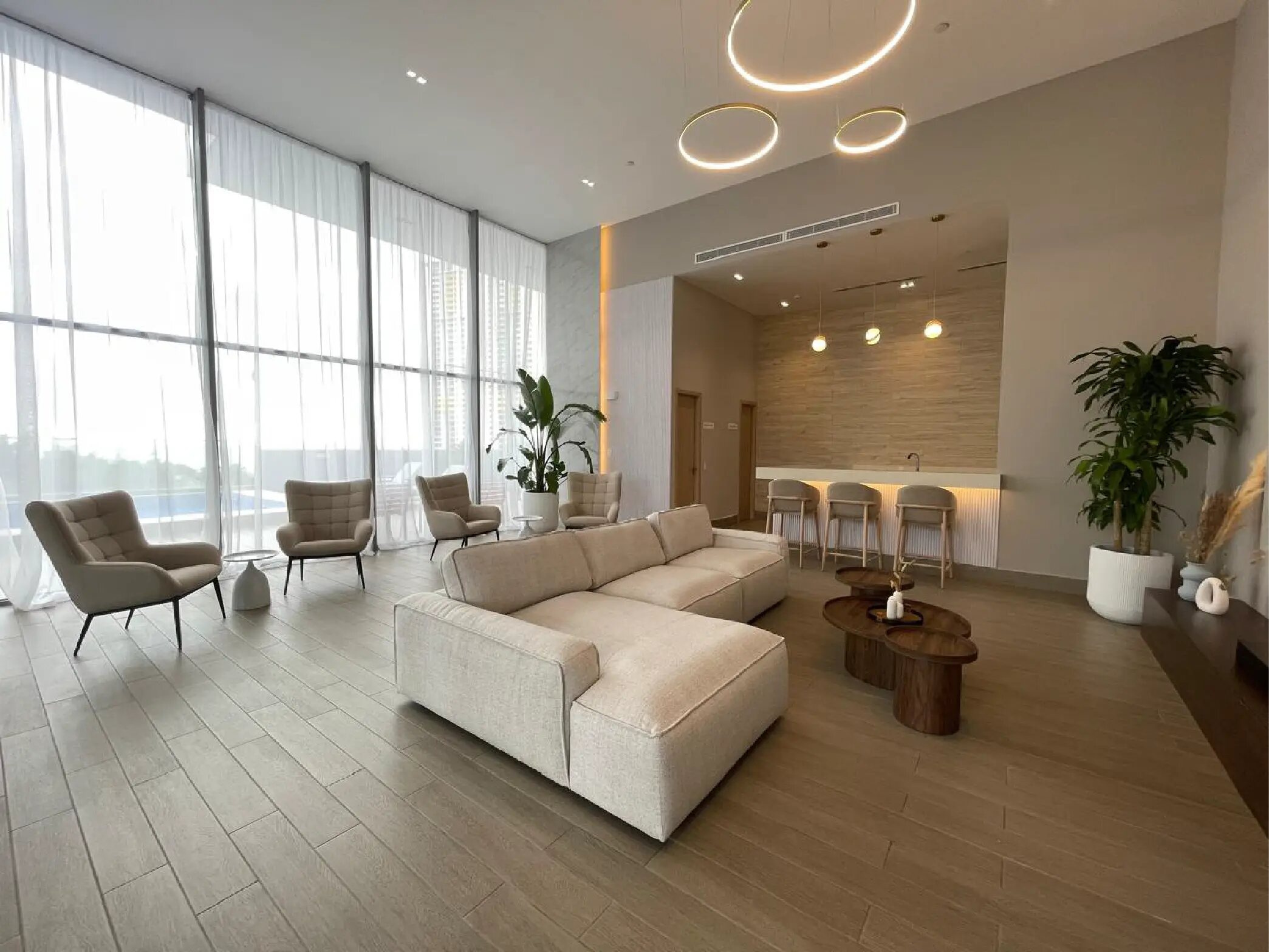 Área social con sala, sillones beige, mesa baja y ventanales amplios.