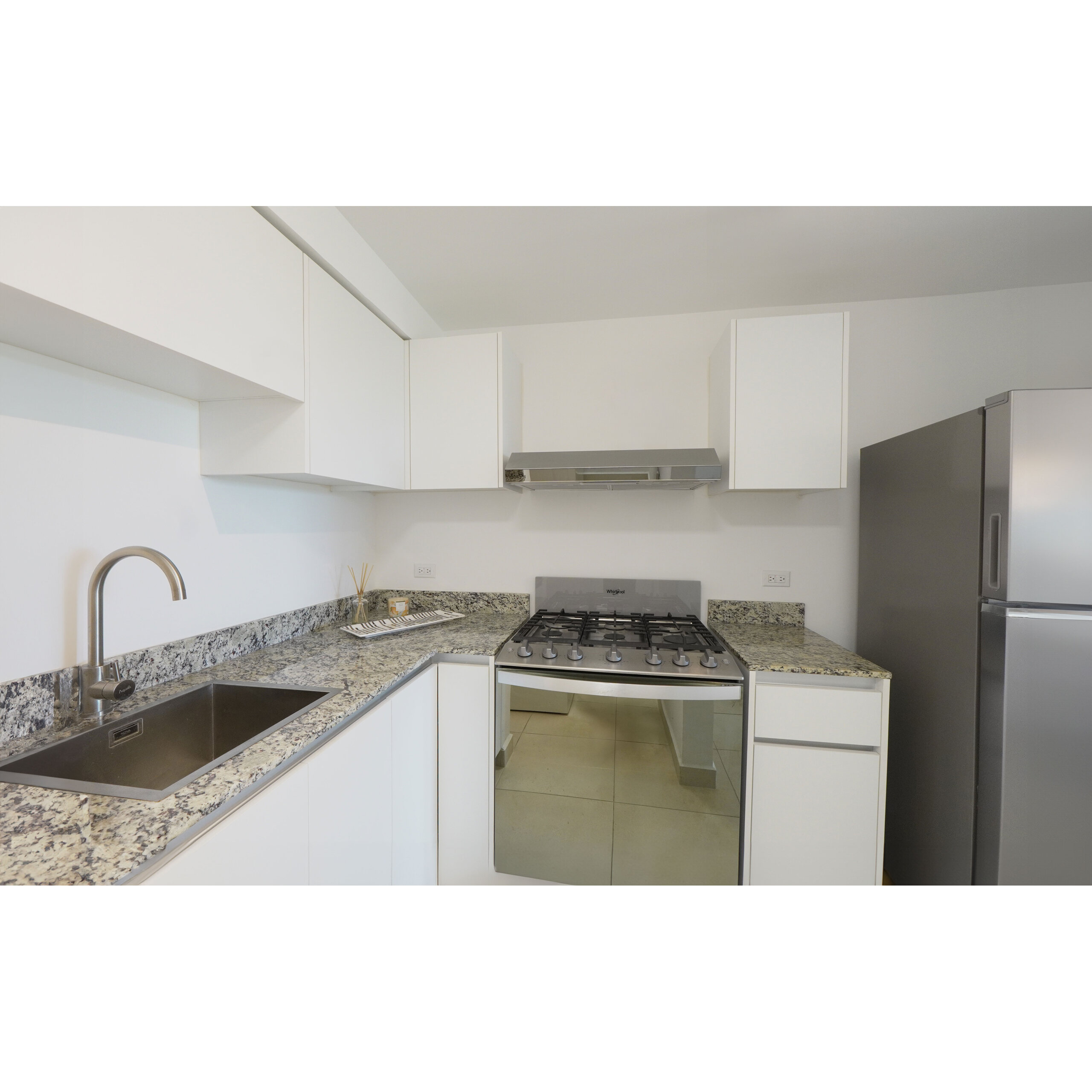 Cocina moderna blanca con encimeras de granito, fregadero, estufa y refrigerador.