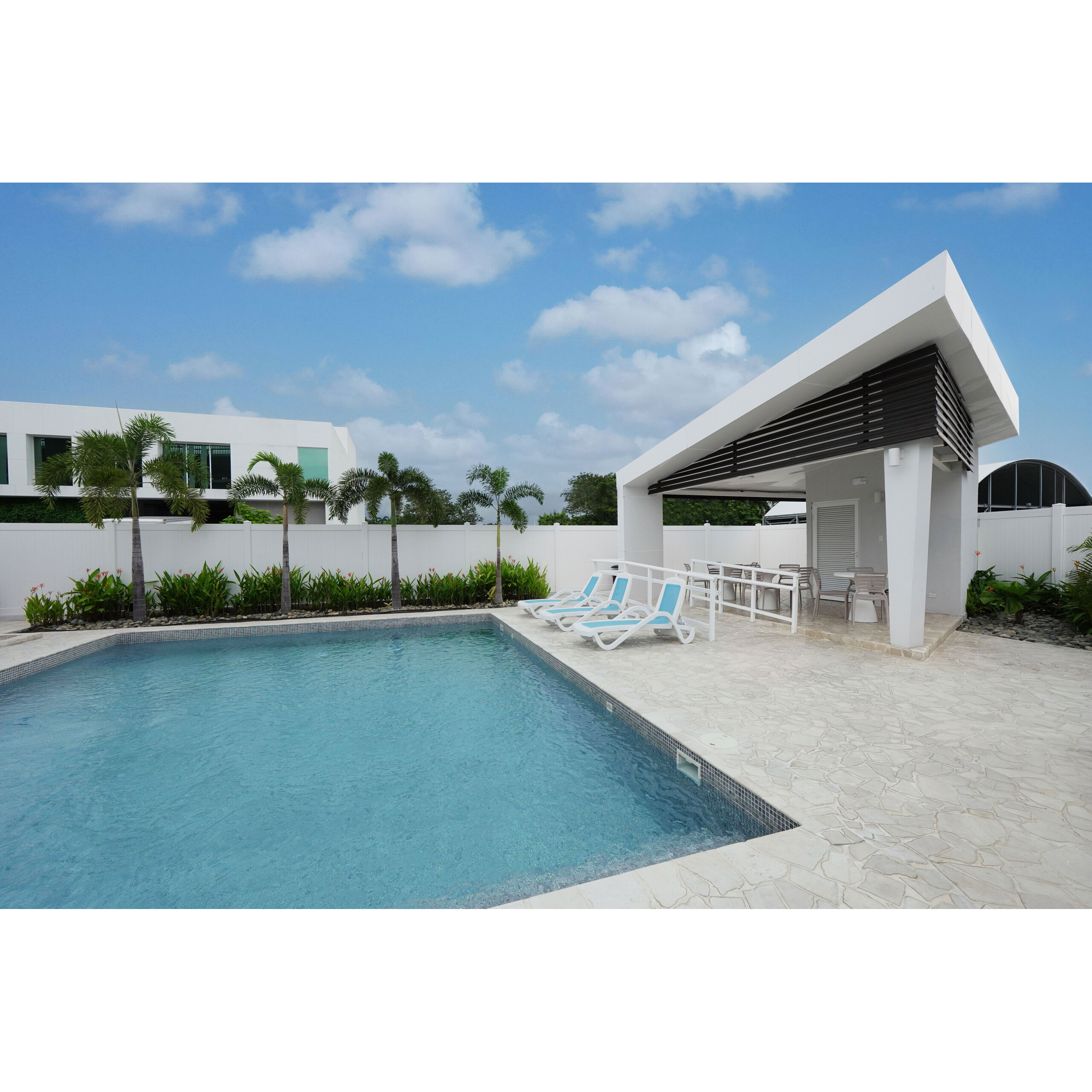 Piscina exterior con camastros y pérgola blanca en área social.
