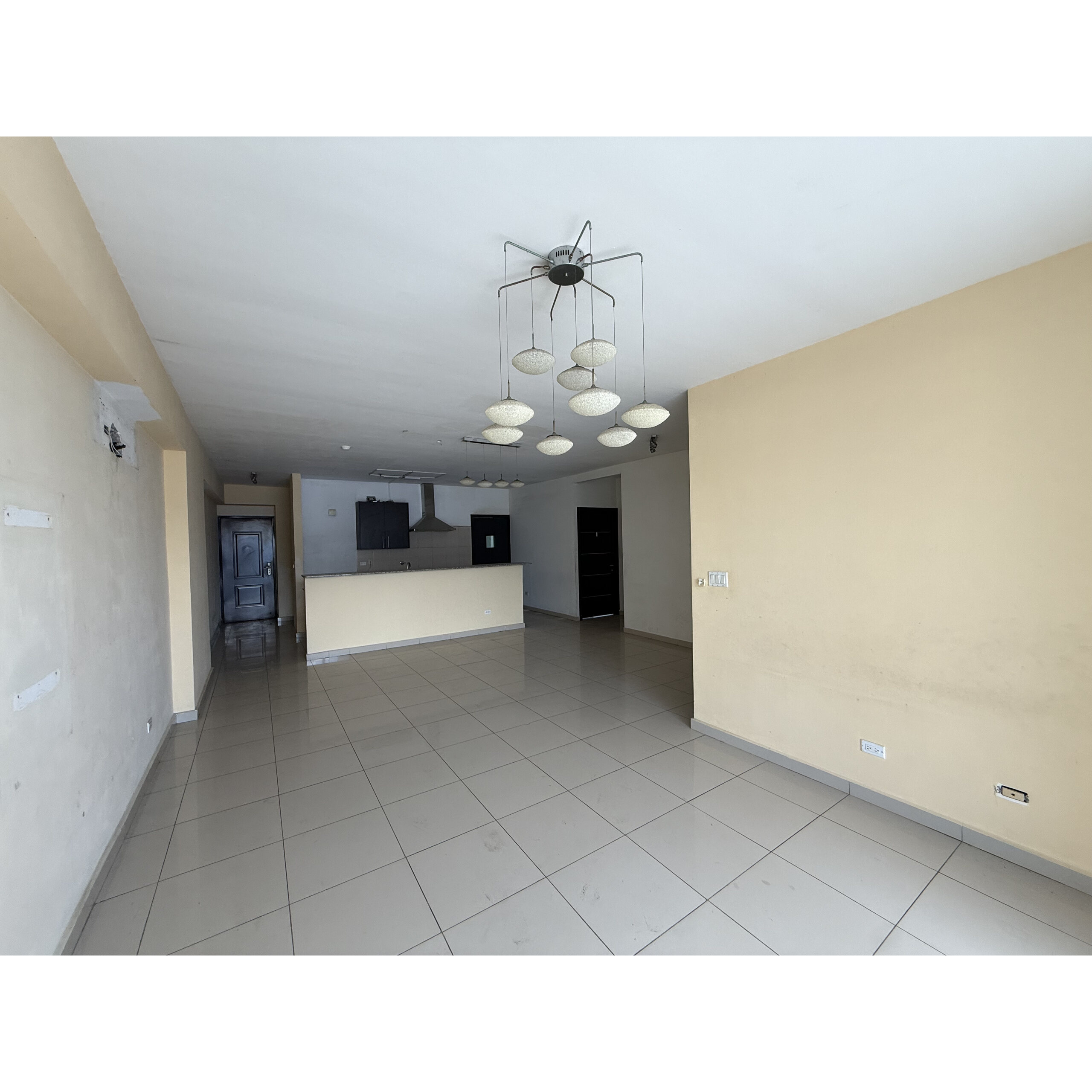 Sala amplia con cocina abierta, piso de baldosas y lámparas colgantes.