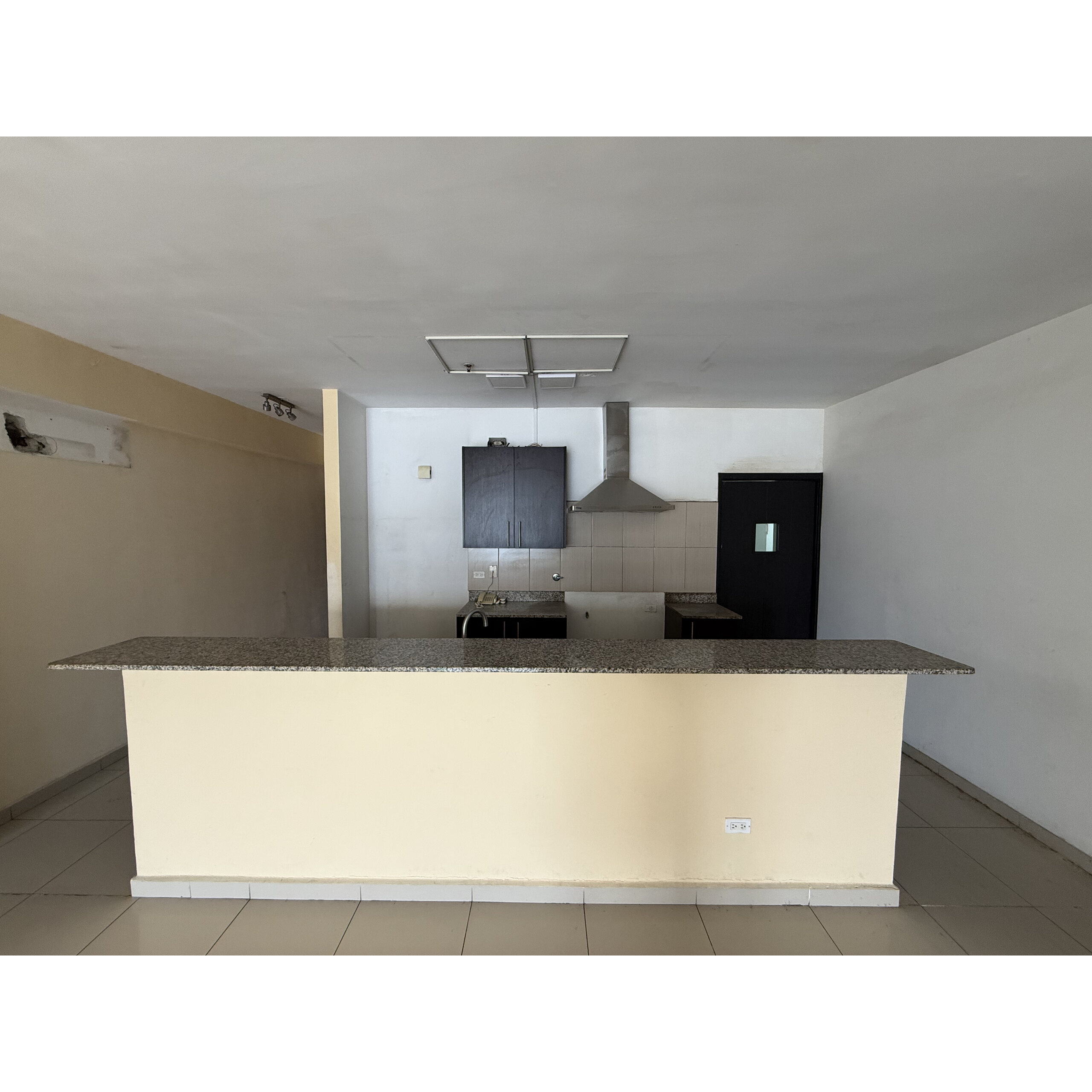 Cocina vacía con isla de granito, gabinetes oscuros y campana extractora.