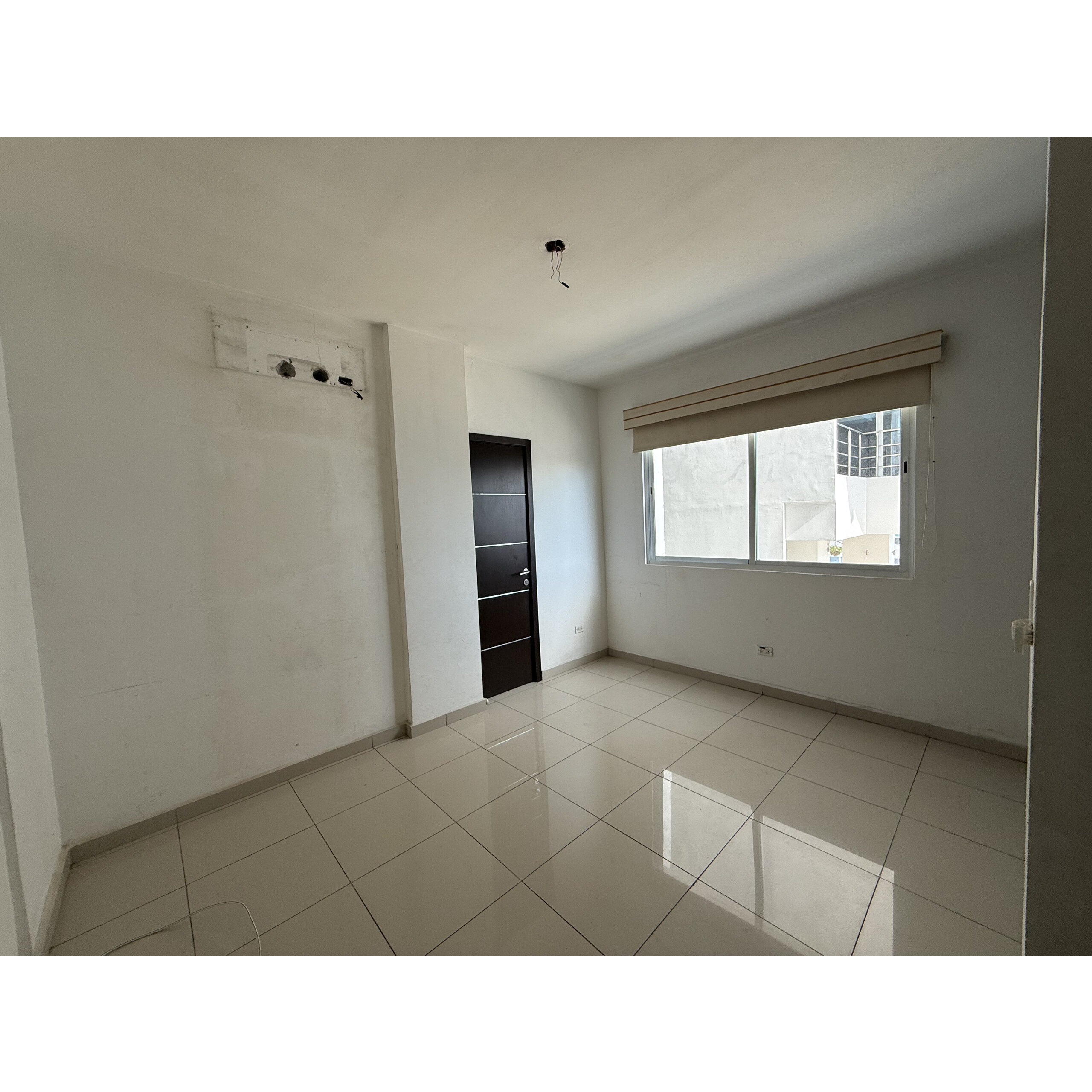 Recámara vacía con piso de loseta, ventana grande y puerta negra.