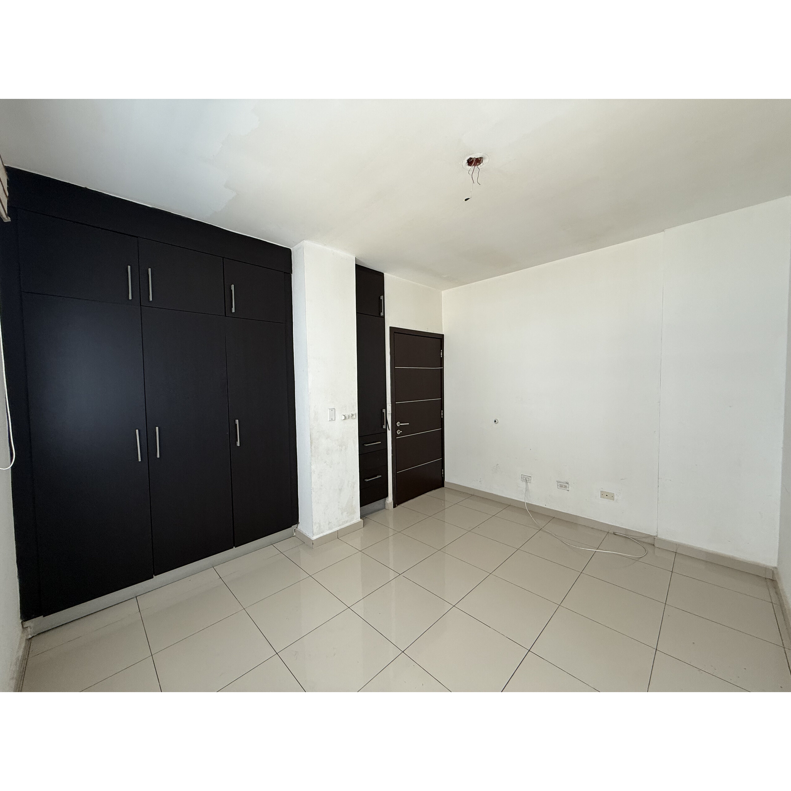 Recámara vacía con clóset negro, puerta de madera y piso de loseta blanca.