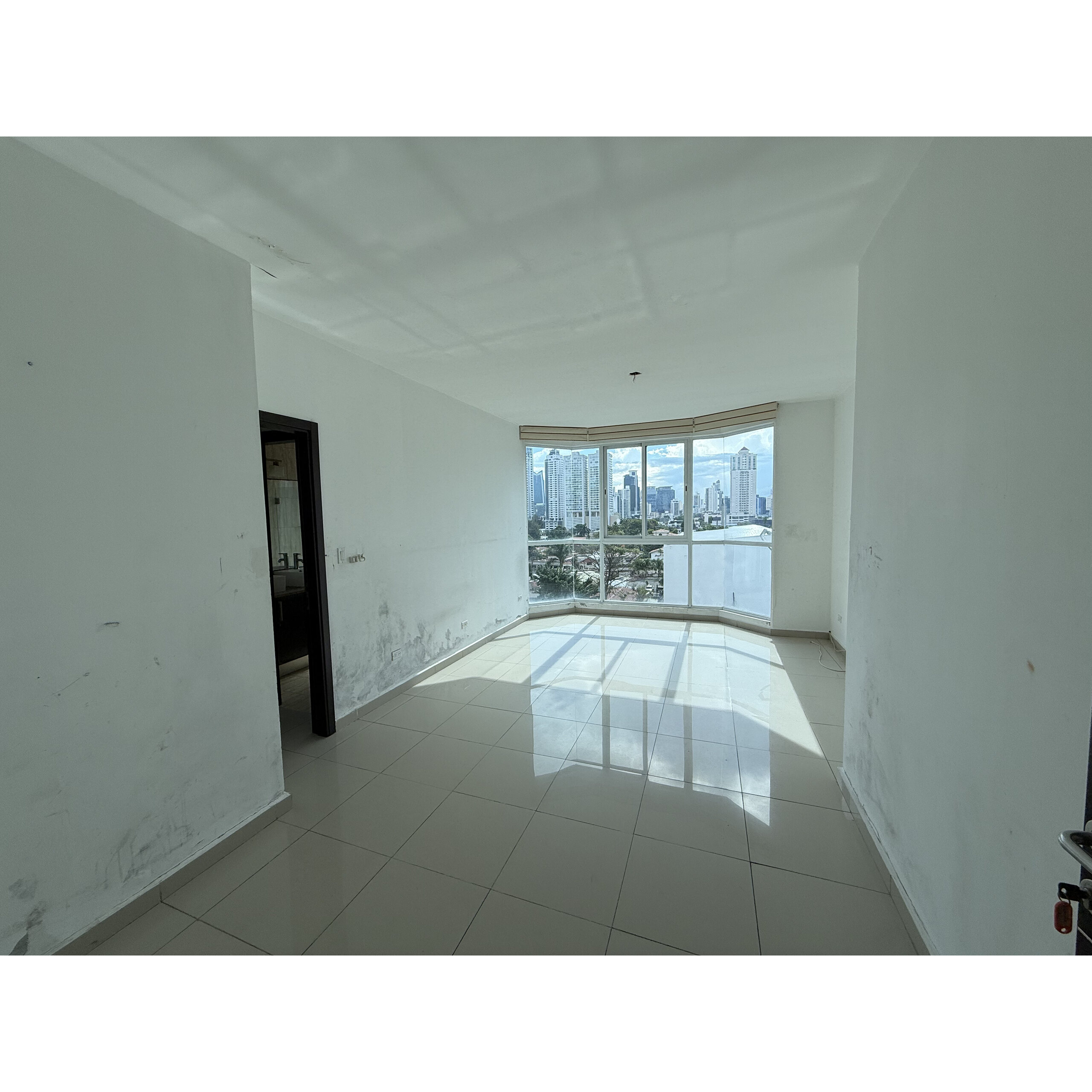 Sala vacía con ventanal y vista a edificios altos.