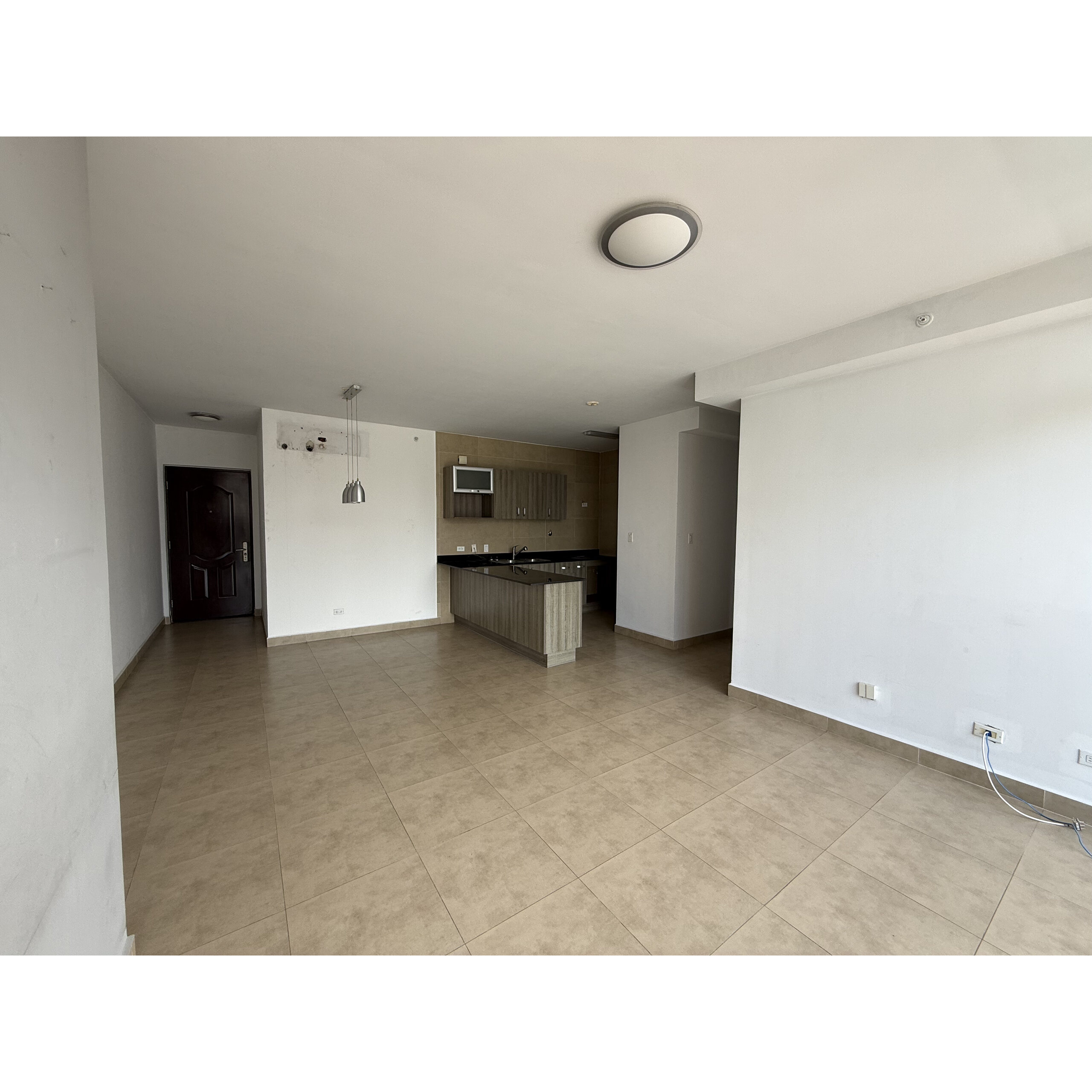 Sala y cocina integradas con piso de cerámica, paredes blancas y barra central.