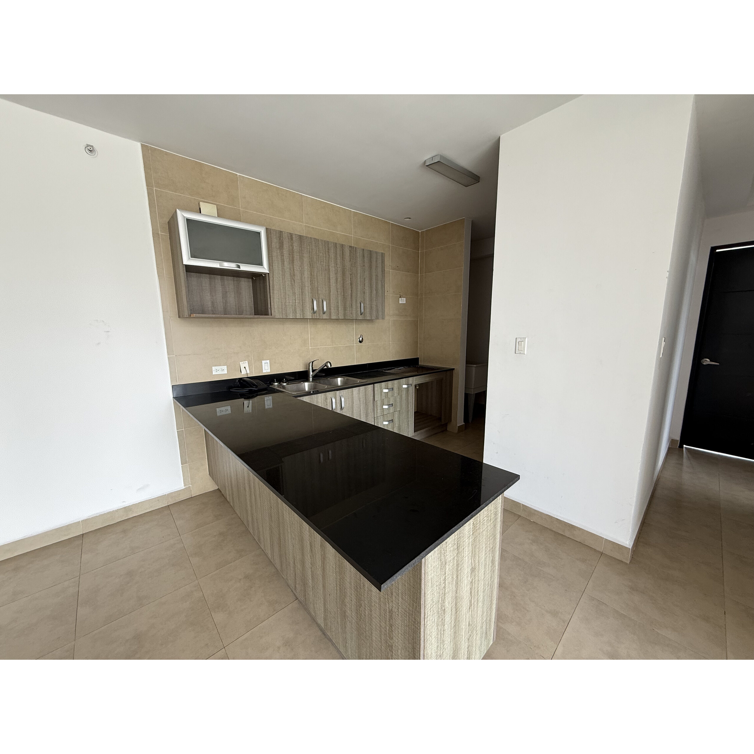 Cocina con barra negra, gabinetes de madera clara y piso beige.