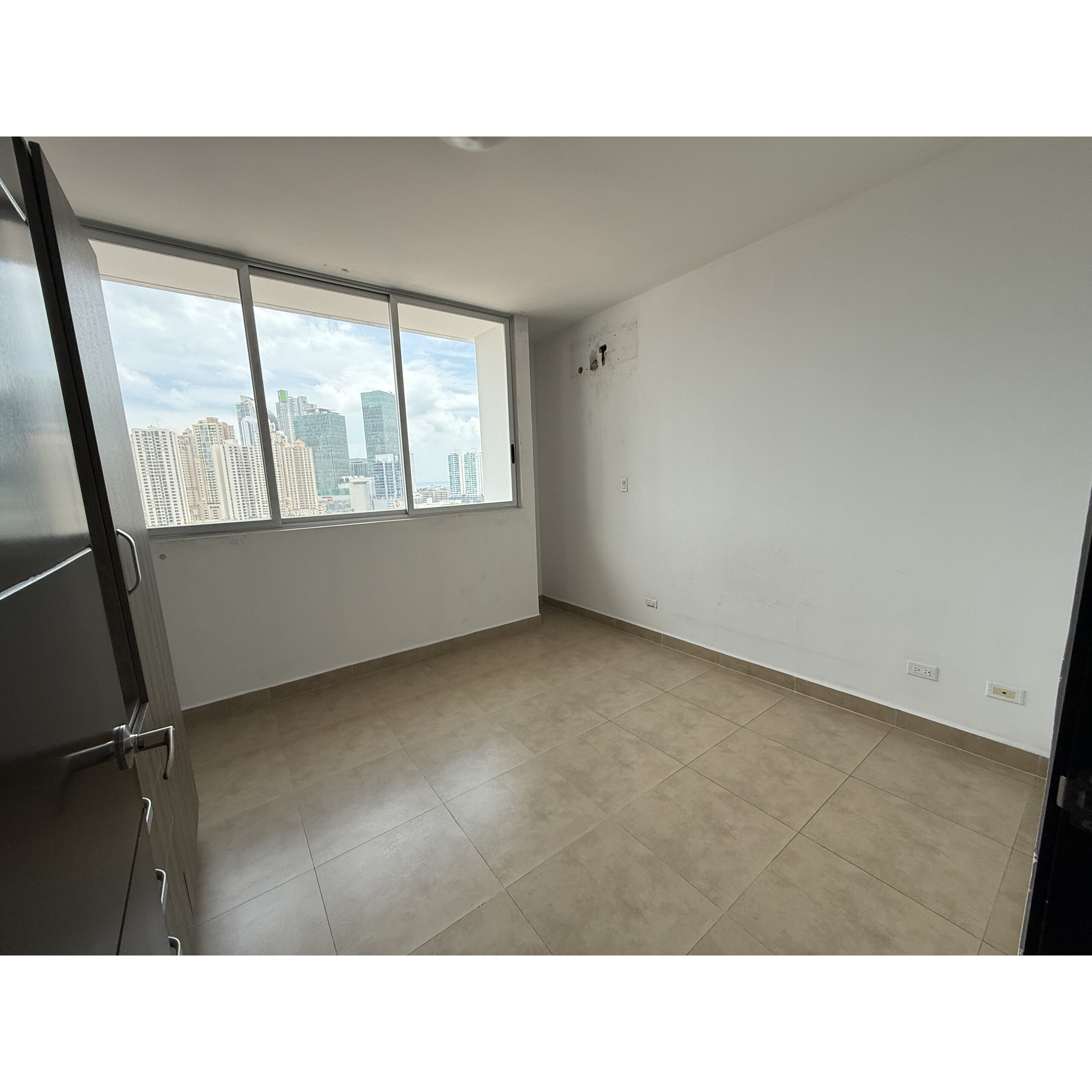Recámara vacía con piso de loseta y vista urbana por la ventana.