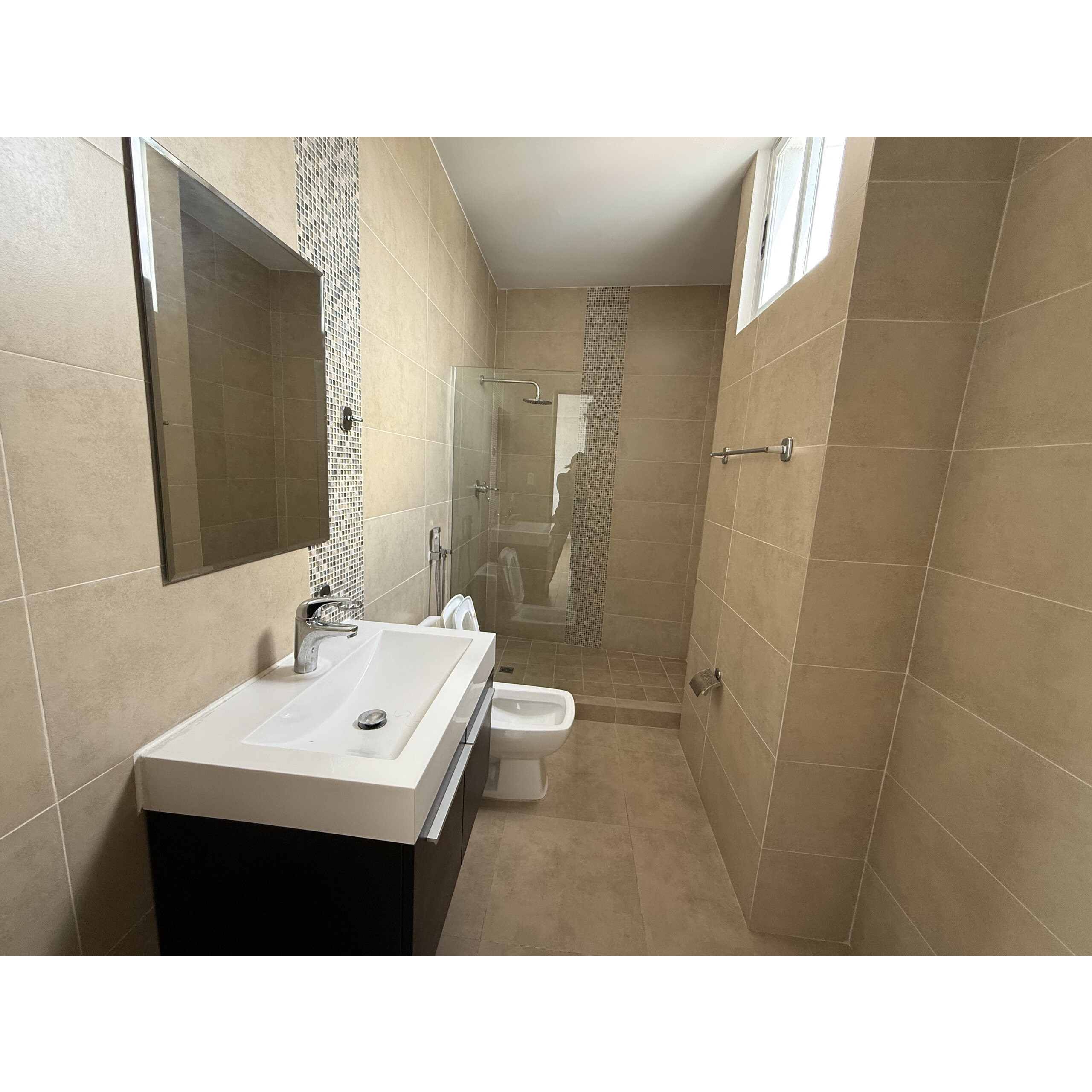 Baño revestido en tonos beige con lavabo, inodoro y regadera de vidrio.