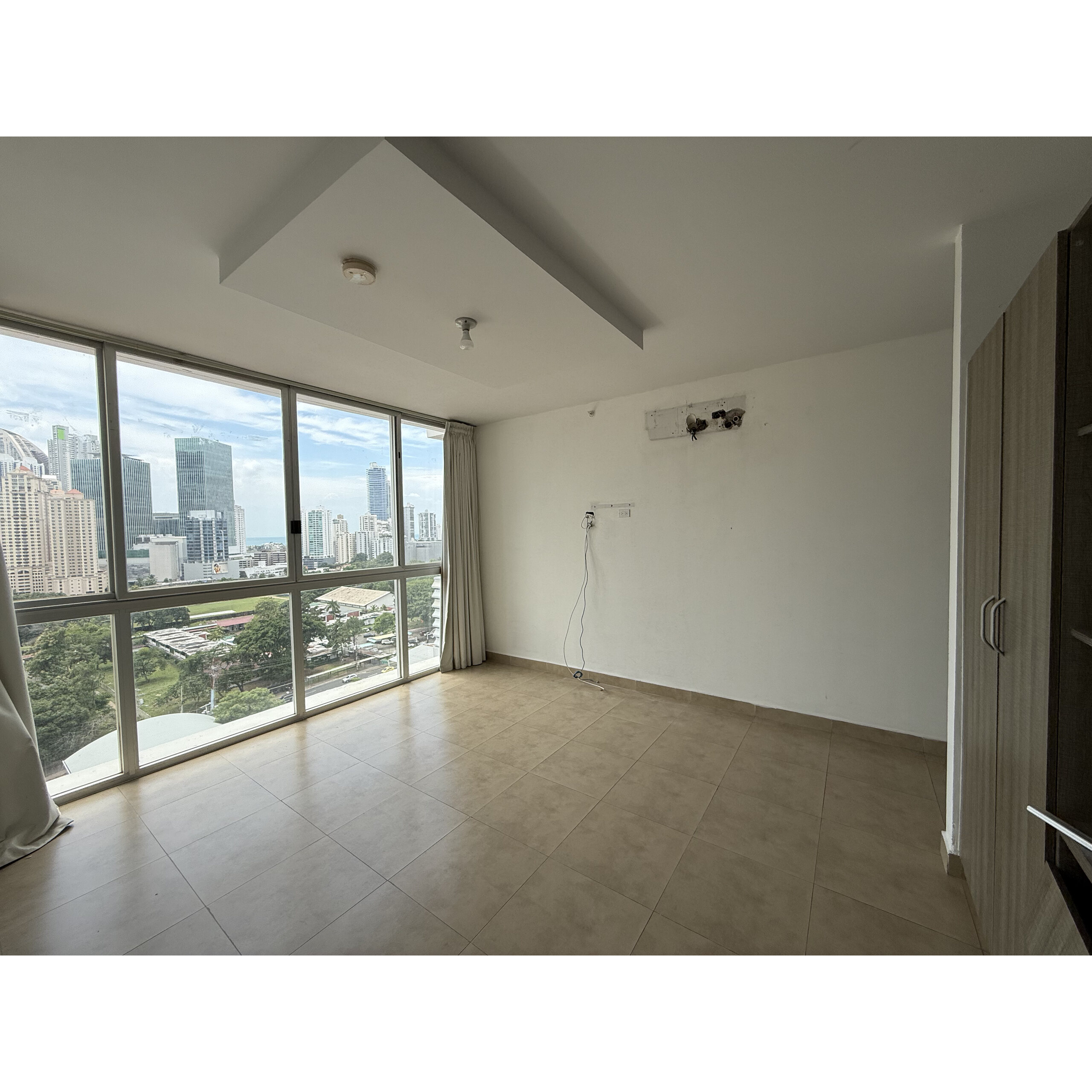 Sala vacía con ventanales grandes y vista urbana.