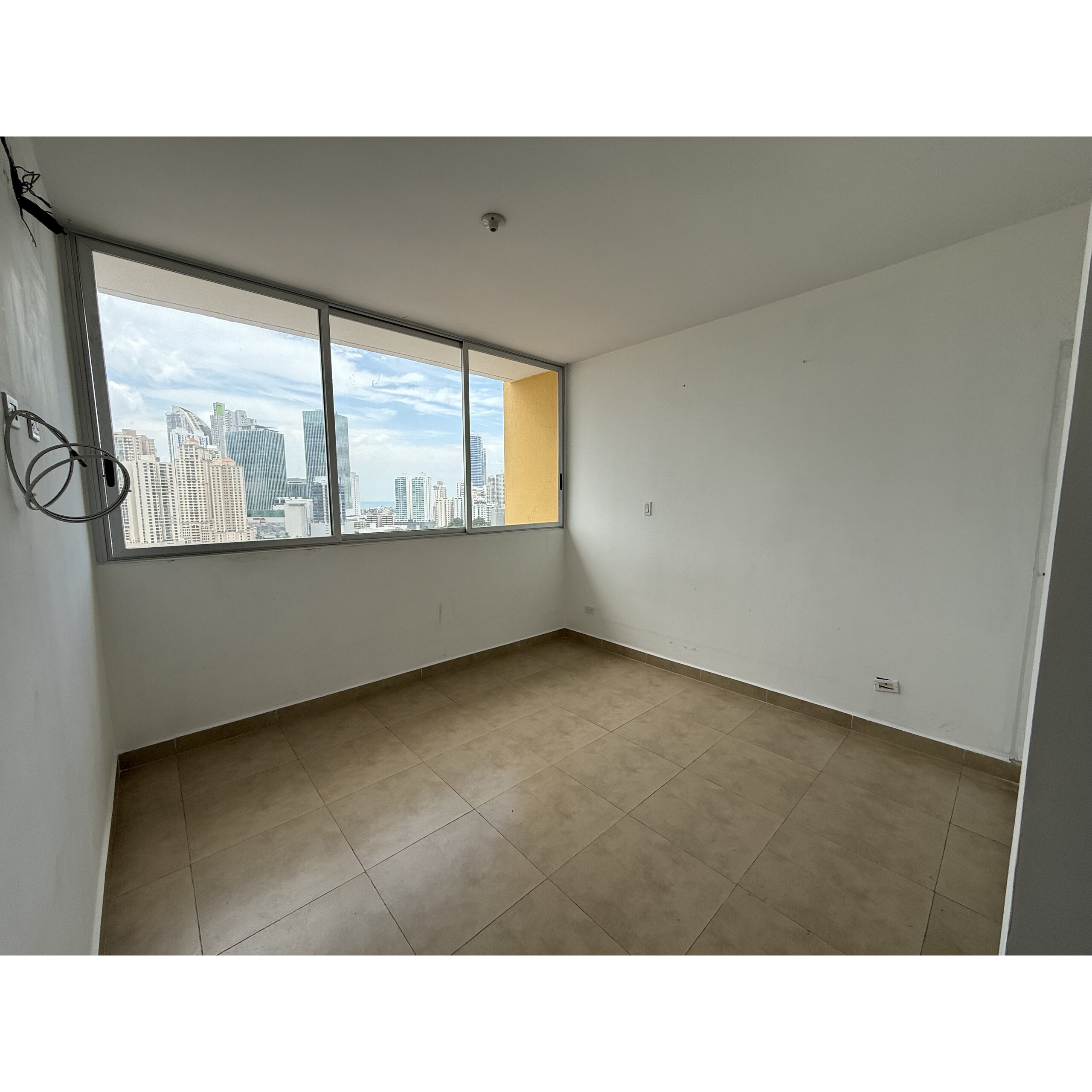 Recámara vacía con ventanal grande y vista urbana.