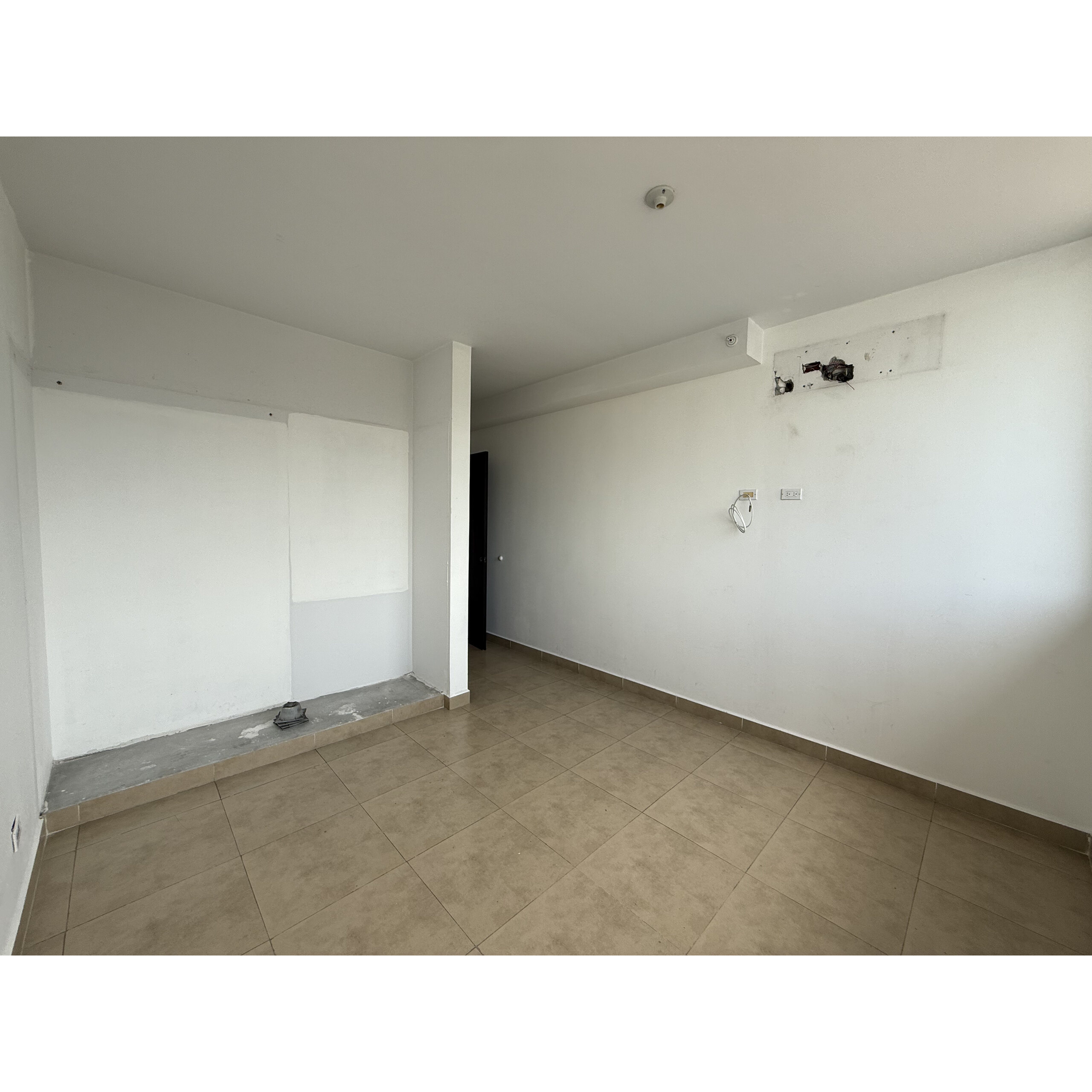 Recámara vacía con piso de loseta beige, paredes blancas y conexiones visibles.